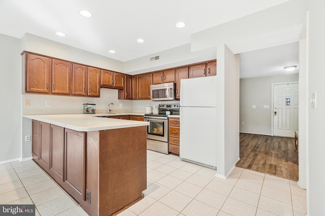 kitchen featuring stainless steel appliances, a peninsula, light tile patterned flooring, and light countertops