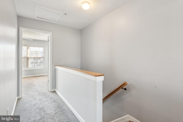 corridor with a textured ceiling, carpet flooring, an upstairs landing, baseboards, and attic access