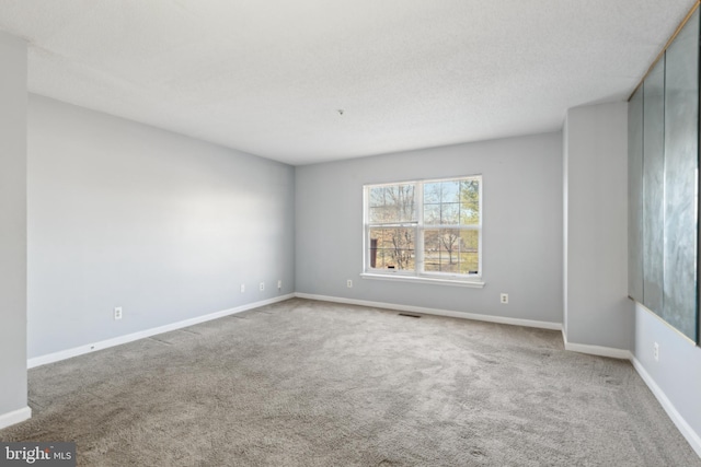 empty room with carpet, visible vents, a textured ceiling, and baseboards