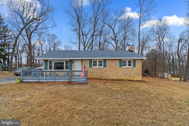 view of front facade featuring brick siding, roof with shingles, a chimney, a front yard, and a wooden deck