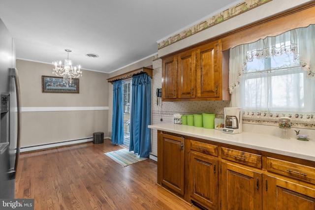 kitchen featuring pendant lighting, a baseboard heating unit, light countertops, brown cabinetry, and crown molding