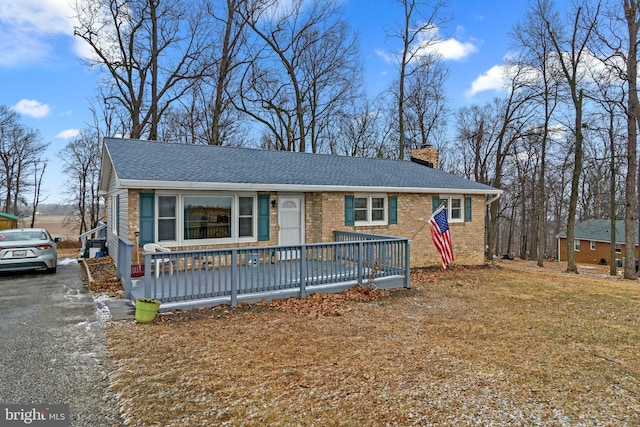 ranch-style home featuring driveway, brick siding, a shingled roof, a chimney, and a front yard