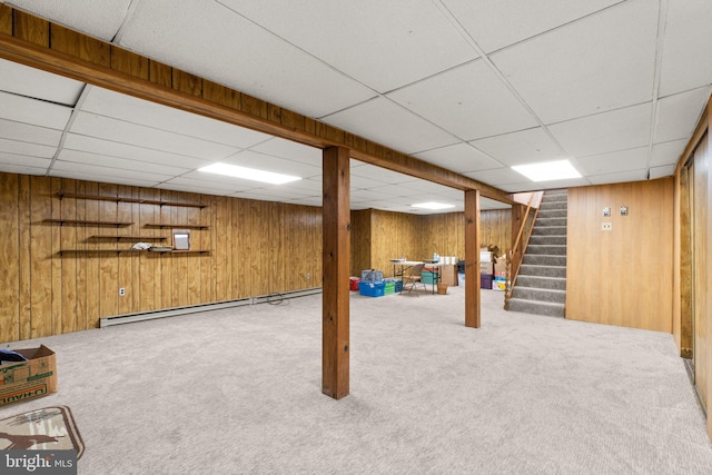 finished basement with a baseboard heating unit, light carpet, wooden walls, a drop ceiling, and stairs