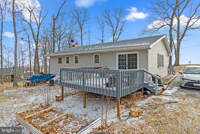 snow covered property with roof with shingles, a chimney, and a wooden deck