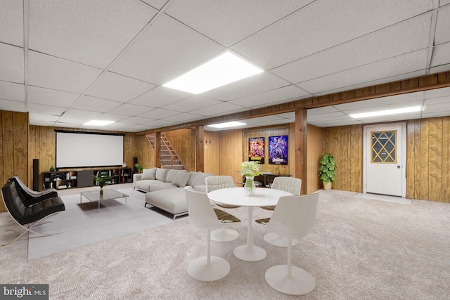 carpeted living area with stairway, a paneled ceiling, and wooden walls