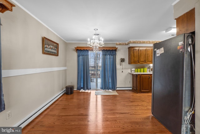 unfurnished dining area featuring a baseboard heating unit, crown molding, a notable chandelier, and wood finished floors