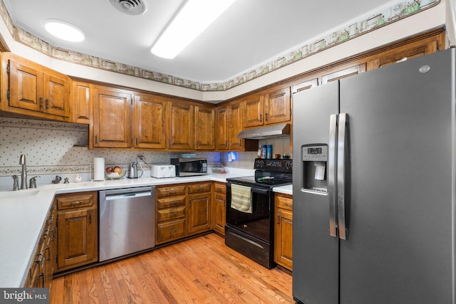 kitchen featuring under cabinet range hood, stainless steel appliances, light countertops, and brown cabinetry