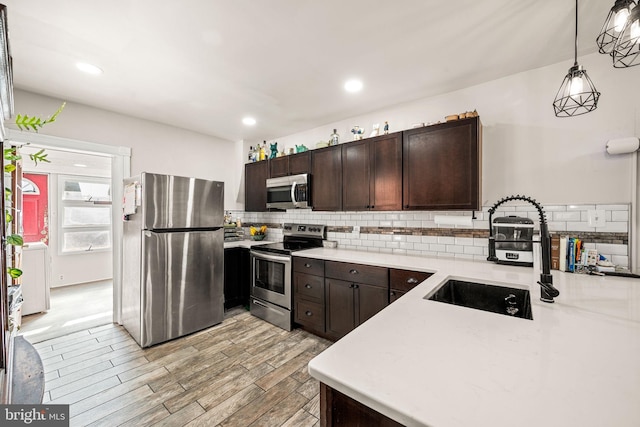 kitchen with stainless steel appliances, a sink, hanging light fixtures, light countertops, and dark brown cabinets