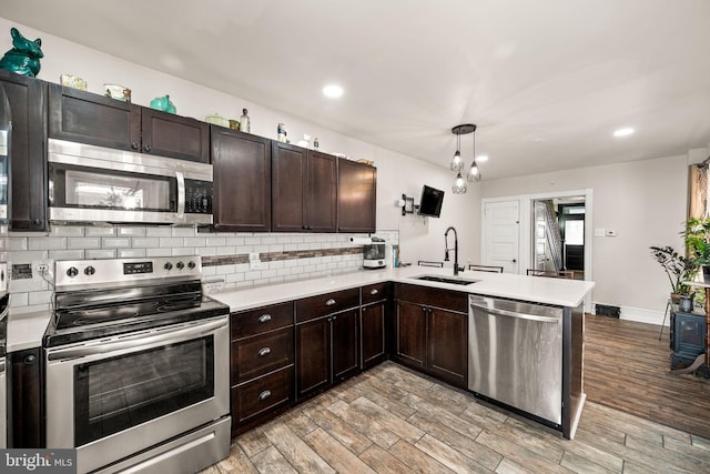 kitchen with stainless steel appliances, a peninsula, a sink, hanging light fixtures, and light countertops