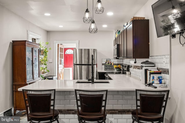 kitchen with a breakfast bar area, light countertops, appliances with stainless steel finishes, hanging light fixtures, and decorative backsplash