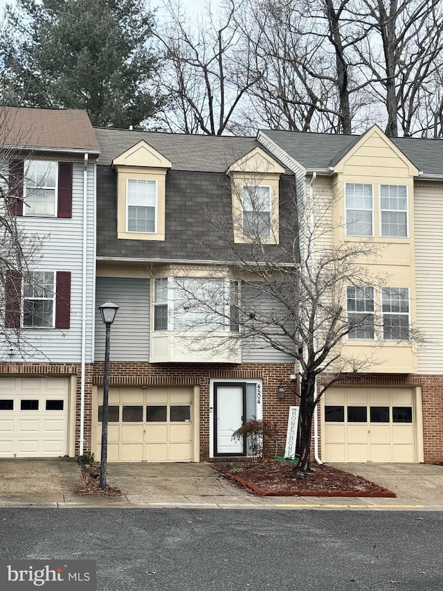 townhome / multi-family property with a garage, brick siding, a shingled roof, and driveway