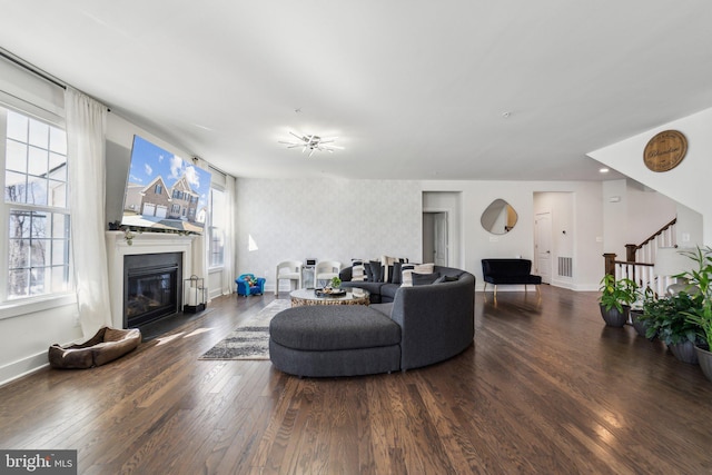 living area featuring dark wood-style floors, a glass covered fireplace, baseboards, and stairs