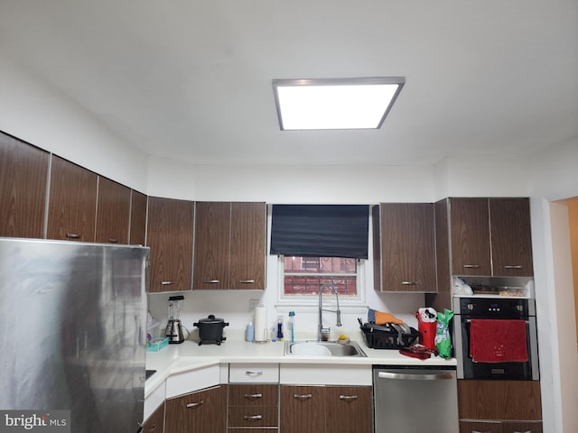 kitchen with stainless steel appliances, dark brown cabinets, a sink, and light countertops