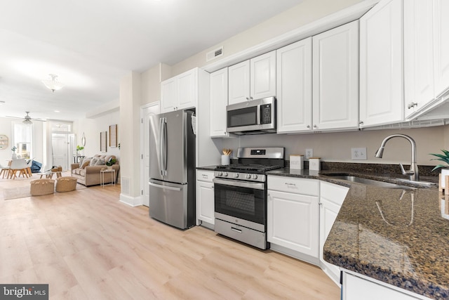 kitchen with stainless steel appliances, sink, white cabinets, and dark stone counters