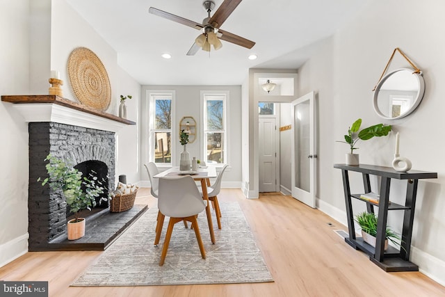 living area with ceiling fan, a stone fireplace, and light wood-type flooring