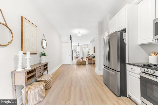 kitchen with stainless steel appliances, dark stone countertops, white cabinets, and light wood-type flooring