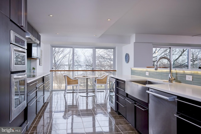 kitchen featuring stainless steel appliances, a wealth of natural light, dark brown cabinets, and tasteful backsplash