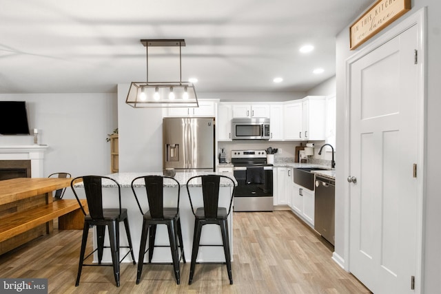 kitchen with decorative light fixtures, sink, white cabinets, a center island, and stainless steel appliances