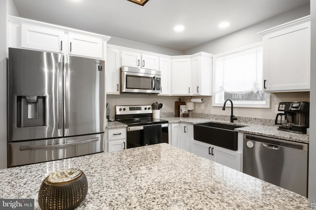 kitchen featuring white cabinetry, appliances with stainless steel finishes, sink, and light stone counters