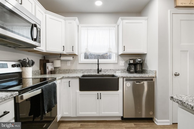 kitchen with white cabinetry, sink, light stone counters, and stainless steel appliances