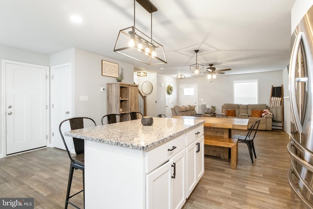 kitchen featuring a breakfast bar area, white cabinetry, a center island, stainless steel refrigerator, and pendant lighting