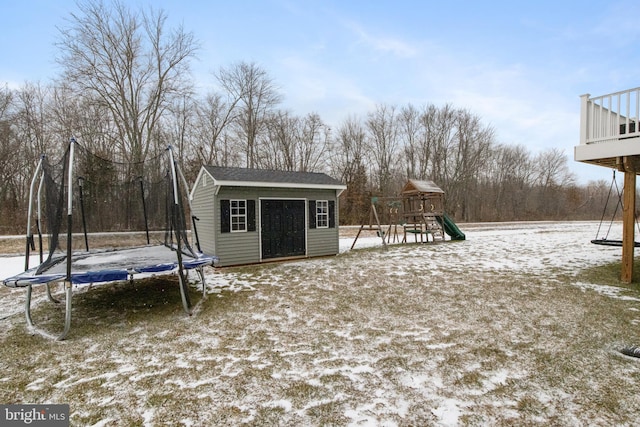 snowy yard with a playground, a trampoline, and a shed