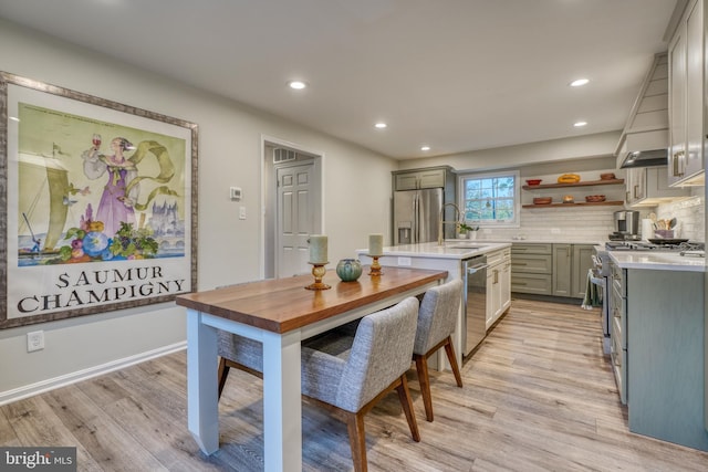 kitchen with appliances with stainless steel finishes, a kitchen island with sink, light countertops, and light wood finished floors