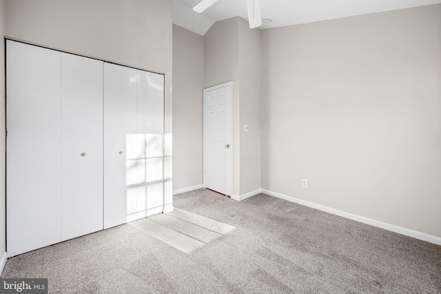 unfurnished bedroom featuring high vaulted ceiling, a closet, carpet flooring, and baseboards