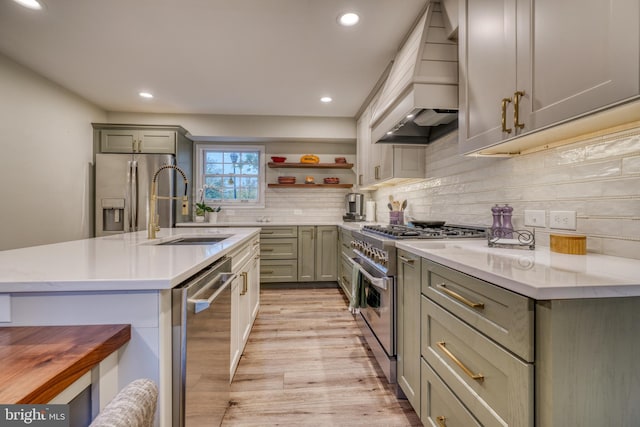 kitchen with decorative backsplash, custom range hood, appliances with stainless steel finishes, light wood-style floors, and a sink