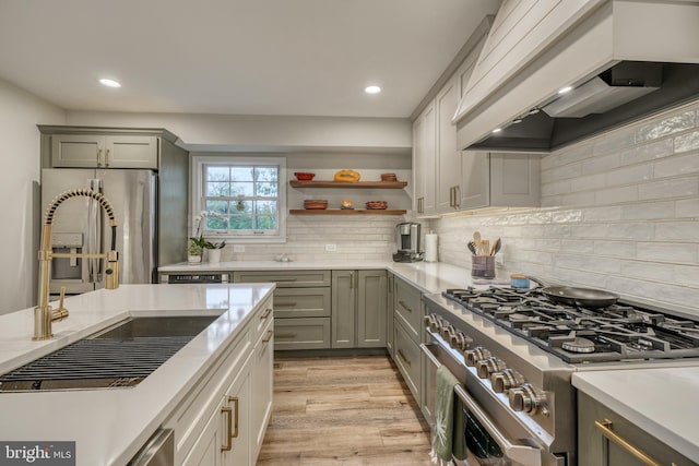 kitchen featuring stainless steel appliances, gray cabinets, custom range hood, and light wood finished floors