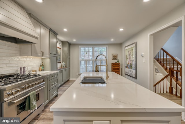 kitchen featuring custom exhaust hood, gray cabinets, high end stainless steel range oven, decorative backsplash, and a sink