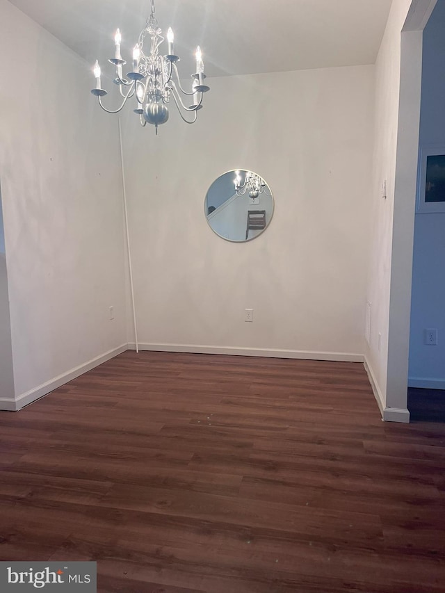 spare room with baseboards, a chandelier, and dark wood finished floors