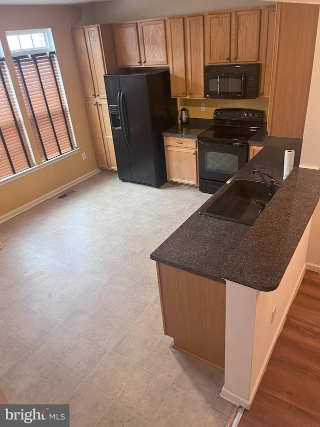 kitchen featuring sink, kitchen peninsula, black appliances, and dark stone counters