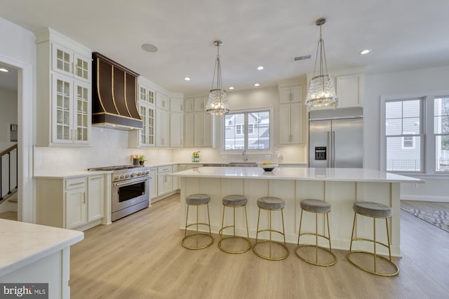 kitchen with a center island, high end appliances, light countertops, glass insert cabinets, and white cabinets