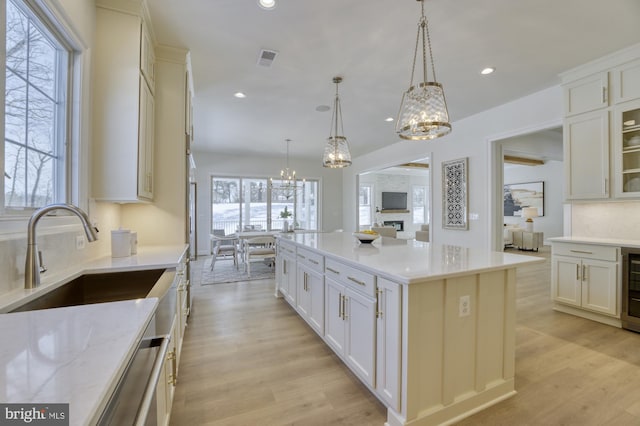 kitchen with light wood finished floors, glass insert cabinets, a center island, hanging light fixtures, and a sink