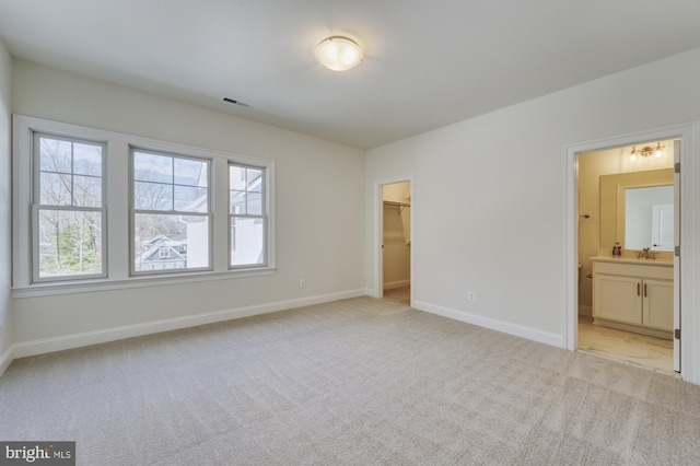 unfurnished bedroom with a walk in closet, light colored carpet, visible vents, a sink, and baseboards