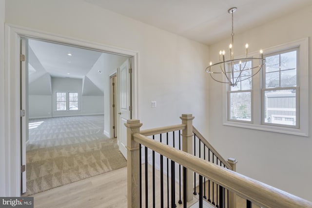 corridor with baseboards, light colored carpet, vaulted ceiling, an upstairs landing, and a chandelier