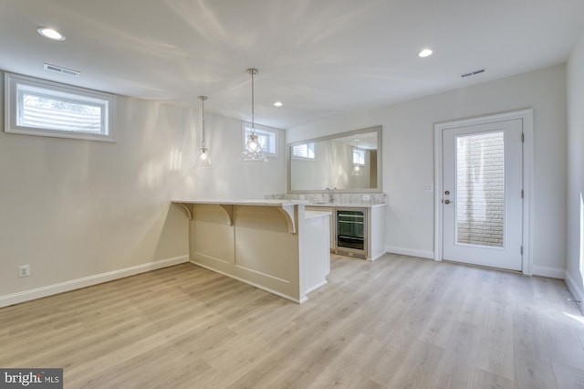 kitchen with a breakfast bar, wine cooler, decorative light fixtures, light countertops, and a peninsula