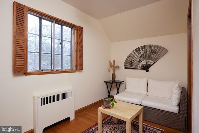 living room featuring lofted ceiling, radiator heating unit, baseboards, and wood finished floors