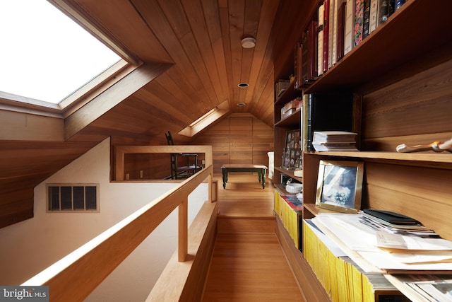 interior space with visible vents, light wood-style floors, wood ceiling, wood walls, and vaulted ceiling with skylight