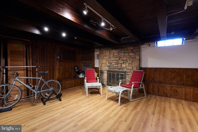 living area featuring wainscoting, light wood-style flooring, beamed ceiling, a stone fireplace, and wood walls