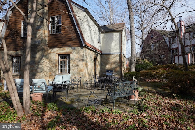 back of house with stone siding, a patio, and a gambrel roof