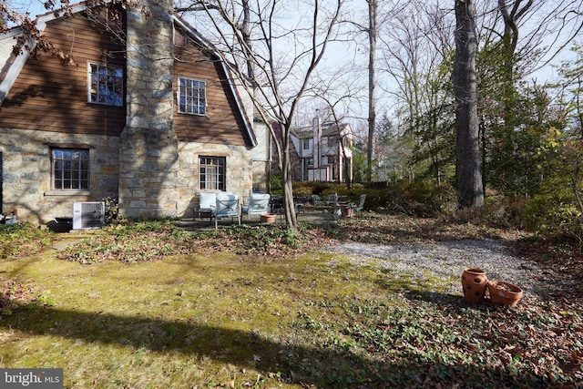 exterior space featuring a yard, stone siding, a gambrel roof, and central air condition unit