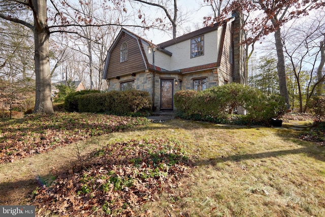 view of front facade featuring a front yard, stone siding, and a gambrel roof