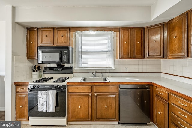 kitchen with brown cabinets, a sink, light countertops, black appliances, and backsplash