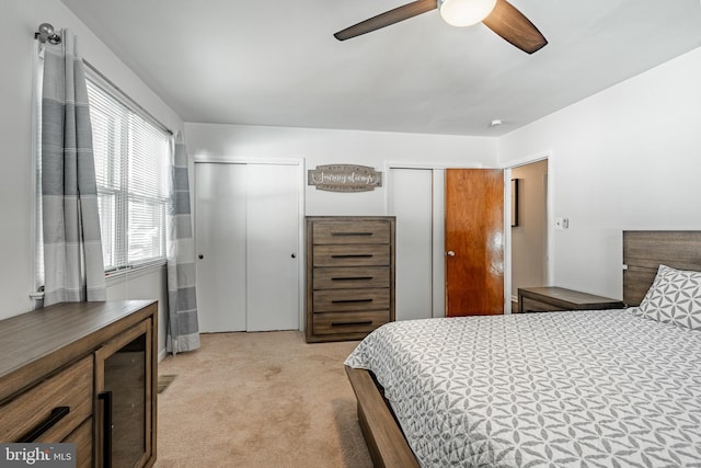 bedroom featuring light carpet, ceiling fan, and two closets