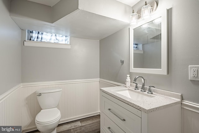 half bathroom with wainscoting, vanity, toilet, and wood finished floors