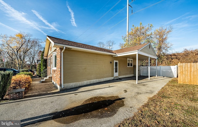 exterior space with a carport, brick siding, driveway, and fence