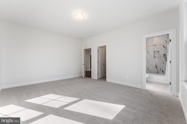 unfurnished bedroom with light colored carpet, ensuite bath, and baseboards