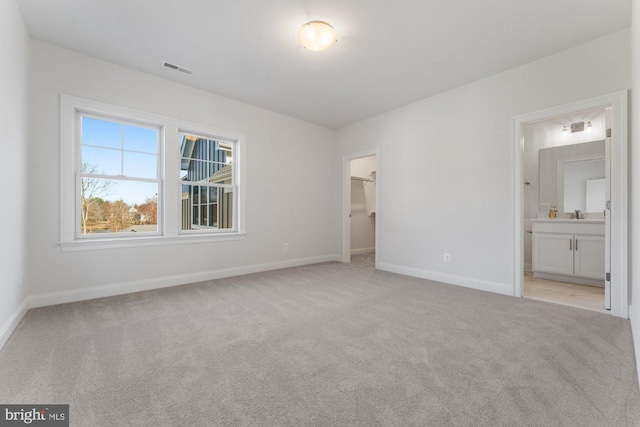 unfurnished bedroom with a spacious closet, baseboards, ensuite bath, visible vents, and light carpet